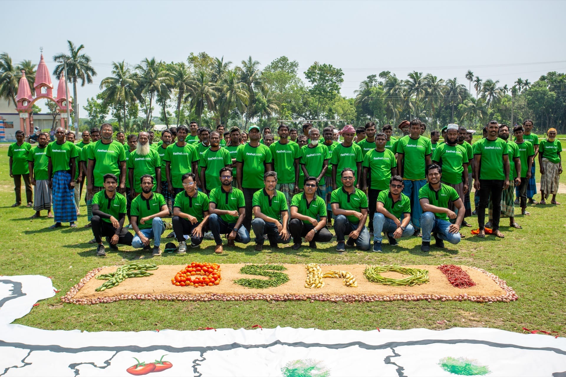 The Fashol company team at an agricultural event, standing and kneeling in Fashol.com green shirts with a vegetable arrangement at their feet.